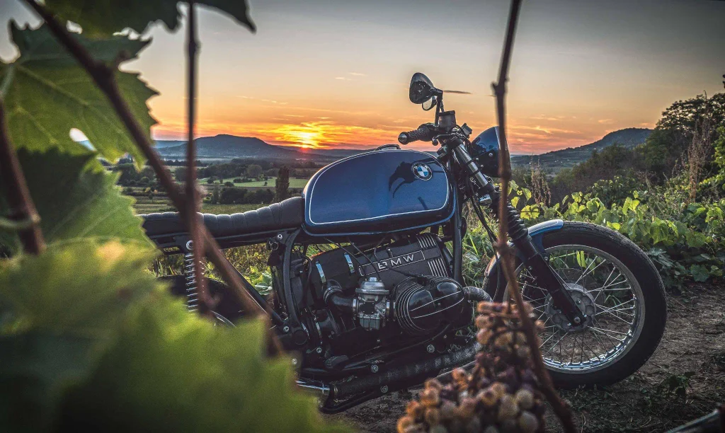 Klasszikus BMW motor szőlőtőkék között a Balaton-felvidéken, a bazalt kúpok fölé leszálló napnyugtával a háttérben – a motorozás és a táj találkozásának tökéletes pillanata